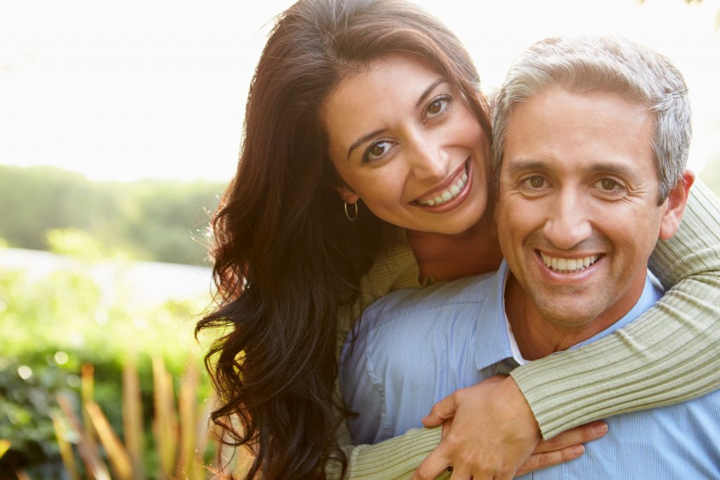 hispanic couple smiling while standing outside woman on man's back