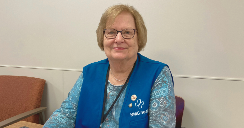 Volunteer sits at desk smiling and greeting hospital patients and visitors