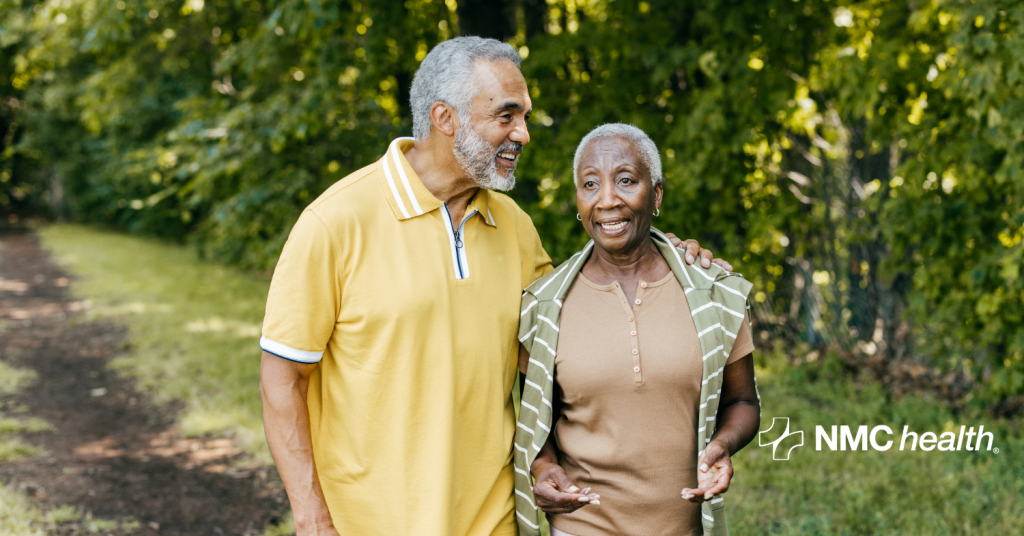 Mature African-American man and woman walking on path with green trees in the background