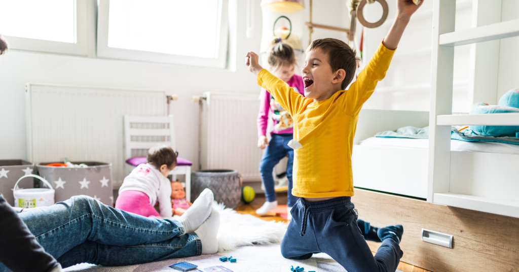 family on floor playing with little boy sitting on his knees with his hands up in the air with an excited expression